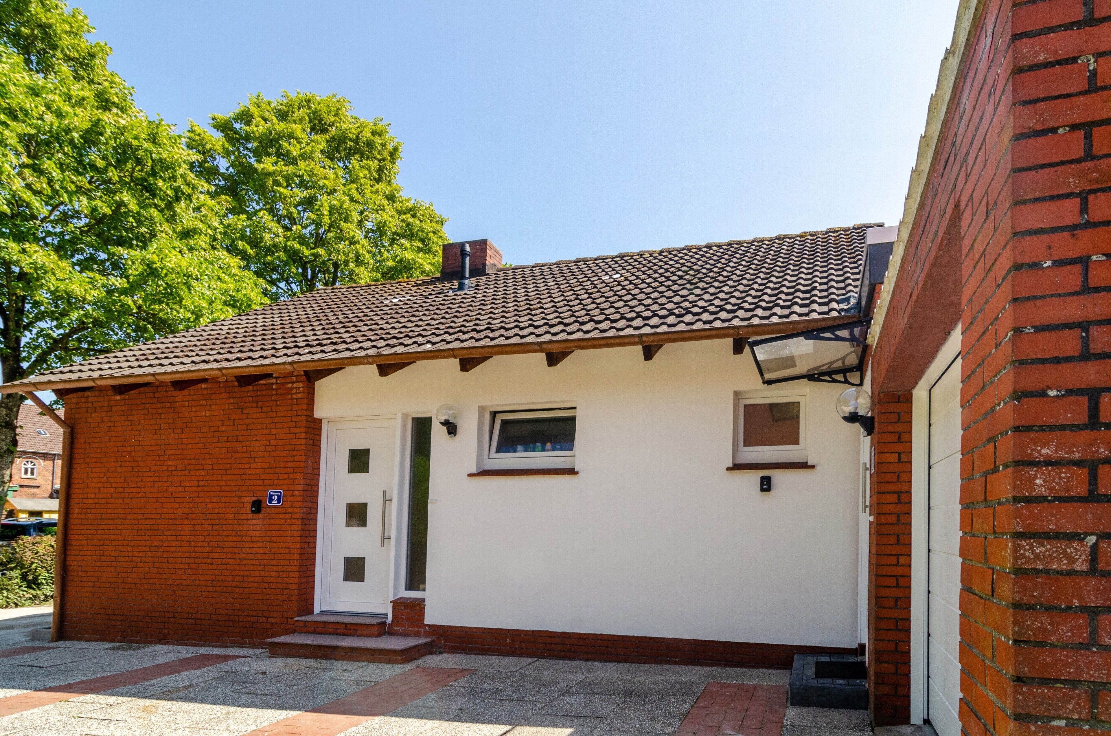 A small, single-story building with a tiled roof, a white exterior, and a brick section on the left.