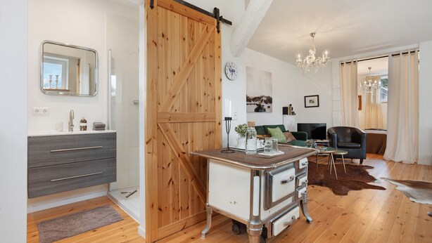 Ein modernes Wohnzimmer mit Holzboden, einer Schiebetür im Scheunenstil, einem weißen Schrank mit Schubladen, einem kleinen Tisch mit einer Vase, einer Kristallleuchter und einem Ledersofa.