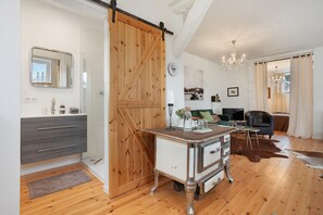 A modern living room with a wooden floor, a sliding barn door, a white cabinet with drawers, a small table with a vase, a chandelier, and a leather sofa. - Apartment "Entenfang" with Private Garden & Wi-Fi (Groß Wokern)
