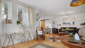 Ein modernes Wohnzimmer mit einem Glastisch, Ledersesseln, einem Esstisch und einem großen Fenster mit Vorhängen.