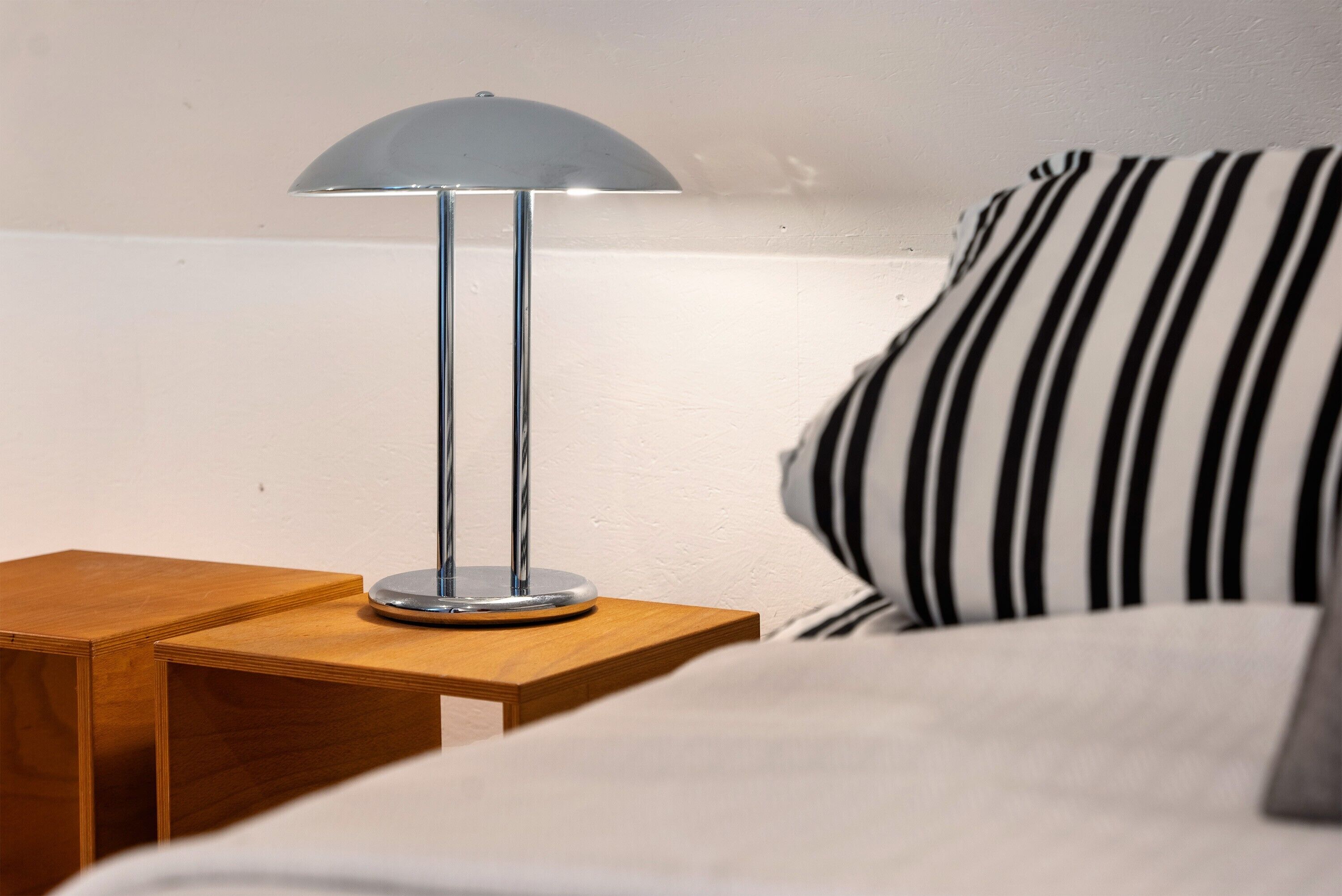 Een nachtkastje met een lamp, een gestreept kussen en een houten ondertafel.