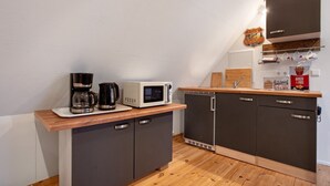 Una cocina compacta con microondas, cafetera y máquina para sándwiches sobre una encimera de madera.