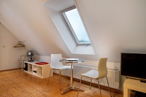 A modern room with a sloped ceiling, a skylight, a round table, two white chairs, a TV, and a radiator. - Apartment "McIntosh" with Private Garden & Wi-Fi (Groß Wokern)