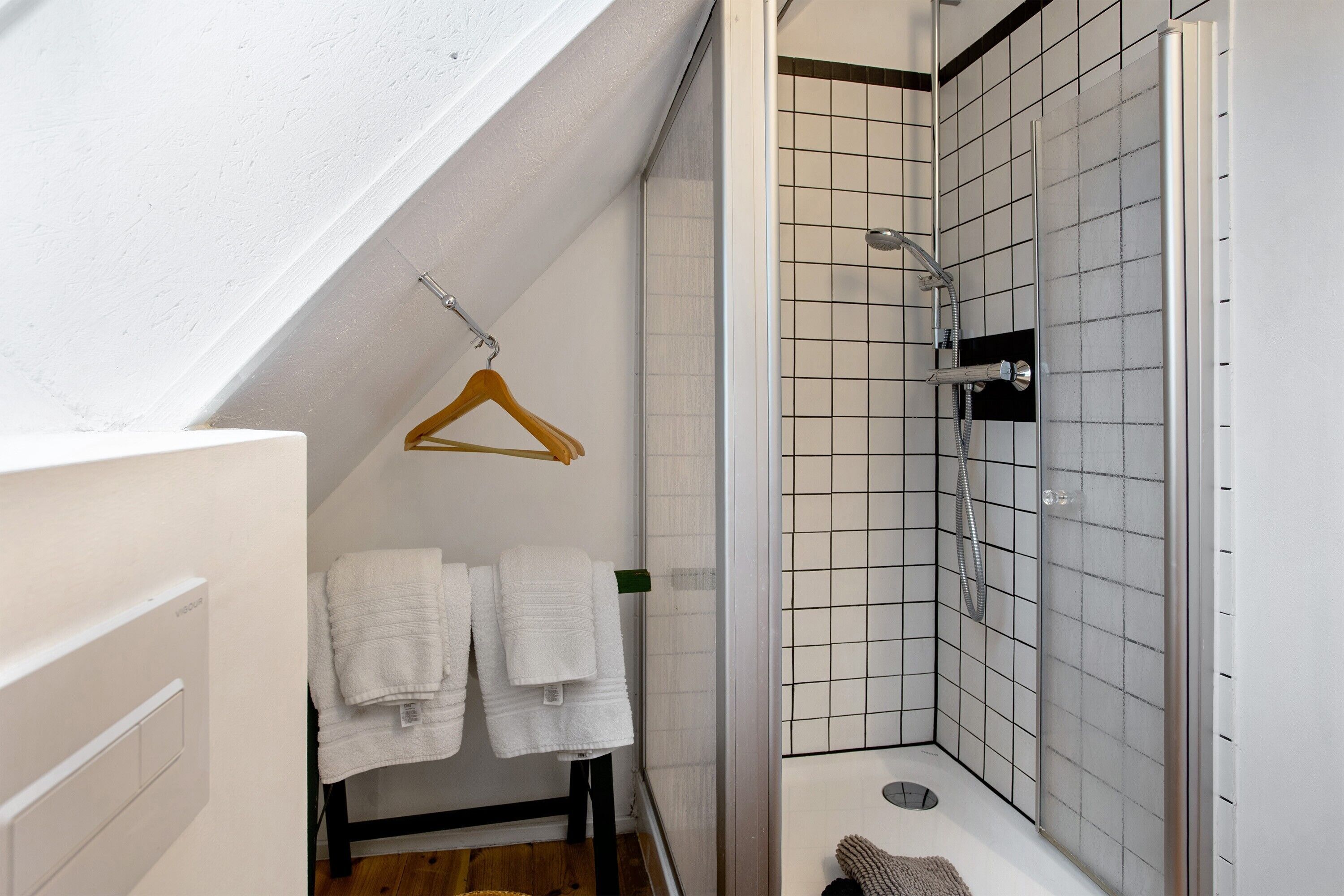 Une salle de bain moderne équipée d’une douche, d’un porte-serviettes et d’un cintre en bois.