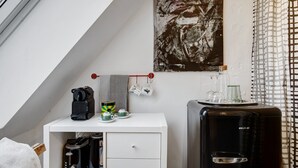 A room with a white dresser, a black refrigerator, a coffee maker, a kettle, and a checkered towel.