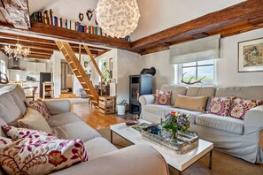 A spacious living area with a fireplace, wooden beams, a staircase, and a view of the outdoors.