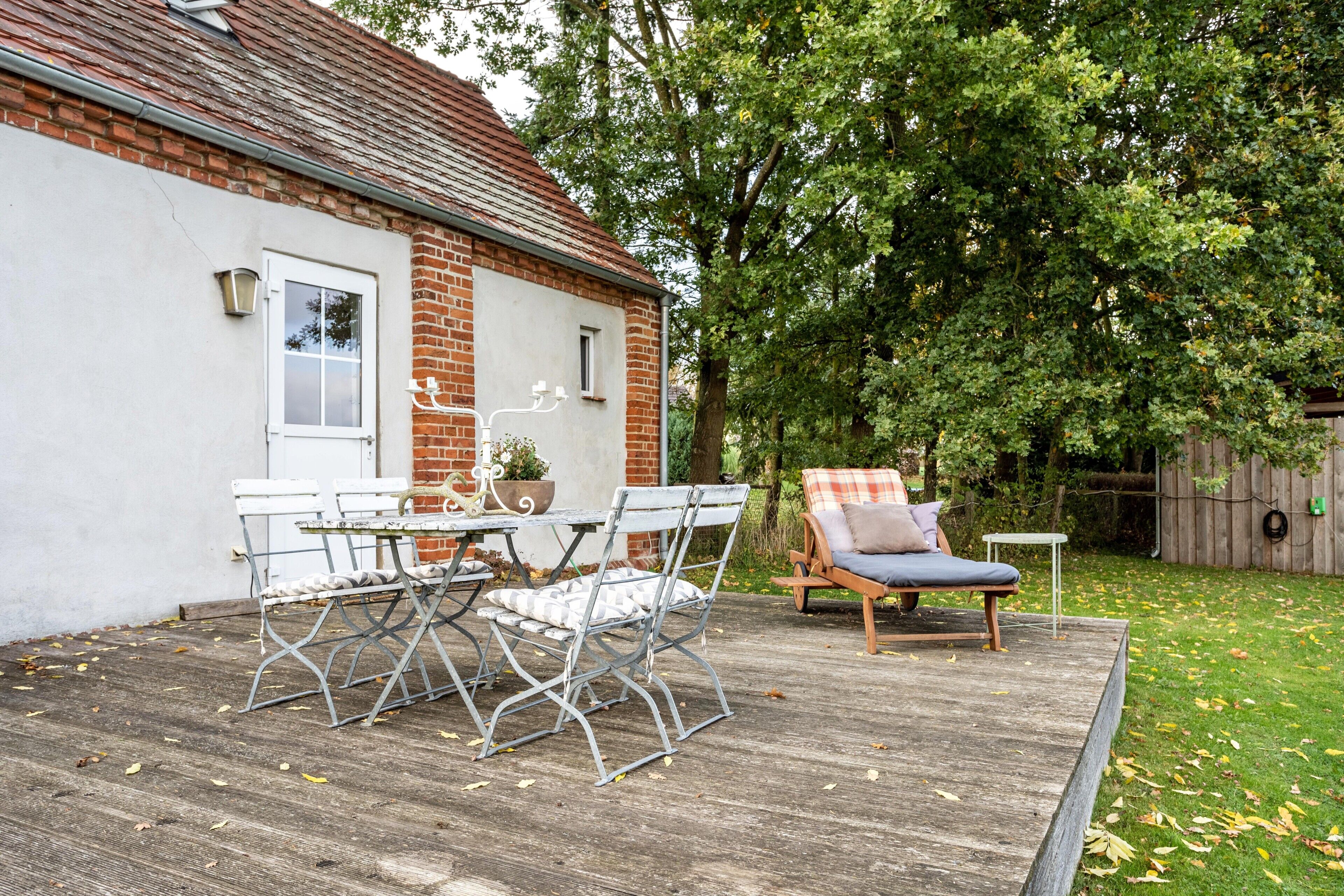 A patio with a table and chairs, a wooden deck, and a garden area with a chair.