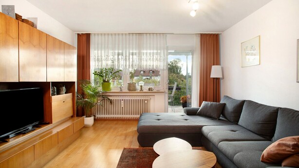 A modern living room with a flat-screen TV, grey sofa, wooden cabinets, and a large window with curtains. - Holiday Apartment "FeWo Schwenck" with Shared Terrace, Shared Garden and Wi-Fi (Kressbronn am Bodensee)