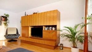 A living room with a wooden entertainment unit, a black leather chair, a large potted plant, and a flat-screen TV. - Holiday Apartment "FeWo Schwenck" with Shared Terrace, Shared Garden and Wi-Fi (Kressbronn am Bodensee)