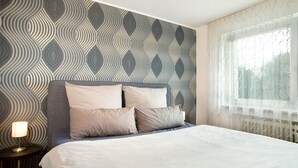 A neatly made bed with a headboard, a bedside lamp, and a patterned wall. - Holiday Apartment "FeWo Schwenck" with Shared Terrace, Shared Garden and Wi-Fi (Kressbronn am Bodensee)