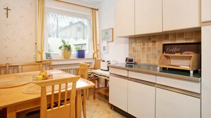 A kitchen with a dining table, chairs, a coffee machine, and a window with curtains. - Holiday Apartment "FeWo Schwenck" with Shared Terrace, Shared Garden and Wi-Fi (Kressbronn am Bodensee)
