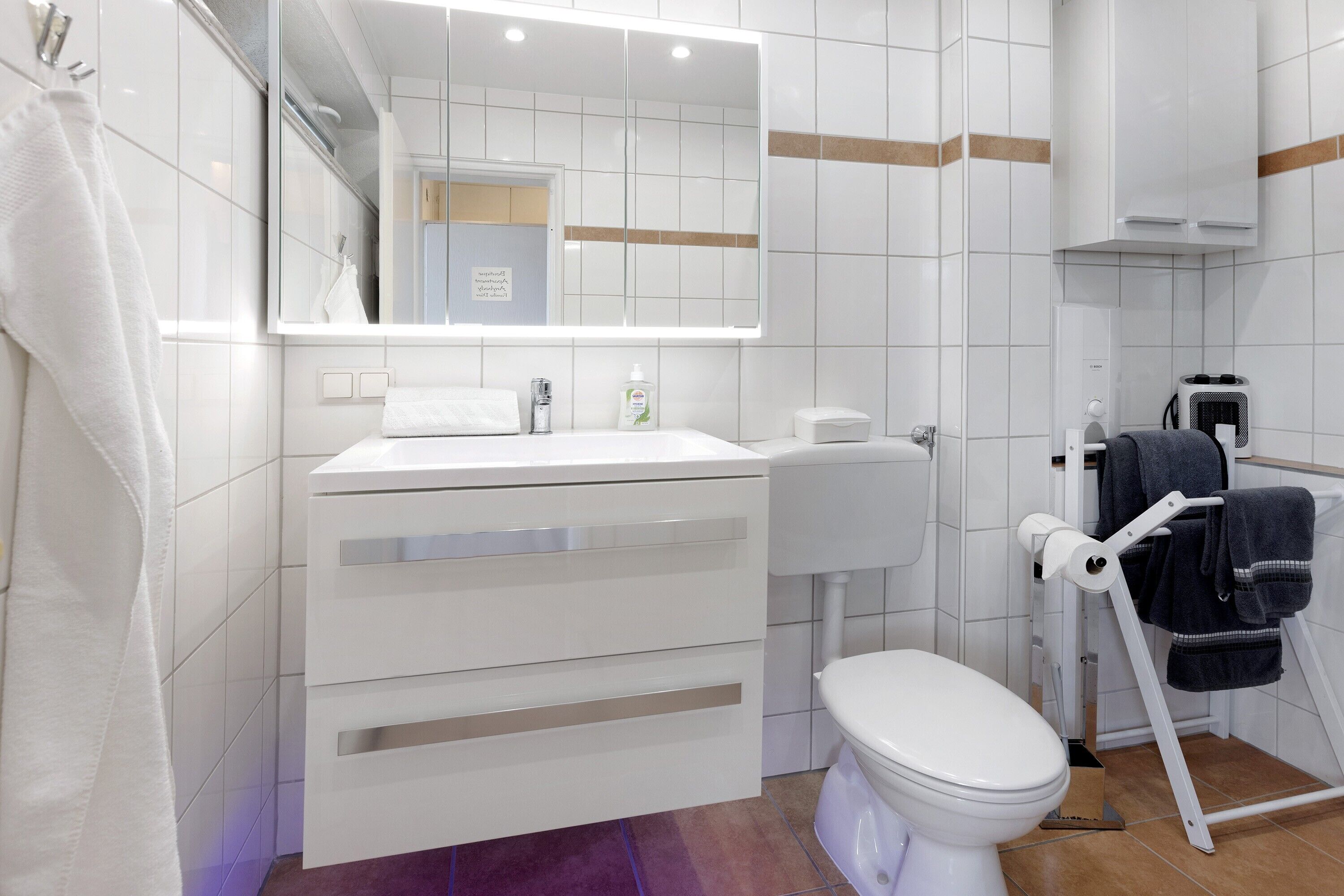 A modern bathroom with a white sink, mirror, toilet, and towel rack.