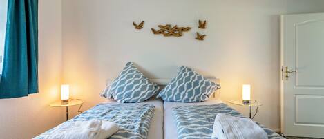 Habitación doble con dos camas, cada una con una colcha estampada y almohadas a juego. Hay luces fijadas a la pared a ambos lados de las camas, y una puerta a la derecha.