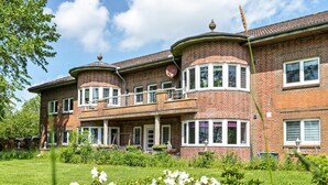 A large brick house with a circular tower, a balcony, and a well-maintained garden.