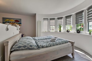 Une chambre à coucher avec un lit, une fenêtre avec des stores, un radiateur et un tableau accroché au mur.