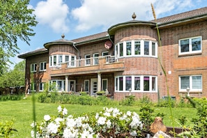 Une maison à deux étages, avec une façade en briques, un balcon et un jardin bien entretenu.