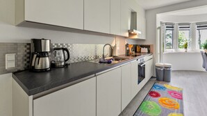 Una cocina moderna con armarios blancos, encimera negra, cafetera y una alfombra colorida.