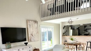 Een ruime woonkamer met een flatscreen-tv, een plafondventilator, een eethoek en een keuken die door een open deur zichtbaar is.
