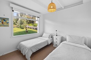 Una habitació amb dos llits individuals, una tauleta de nit, una làmpada, una finestra amb vista a l'exterior i un llum penjant.