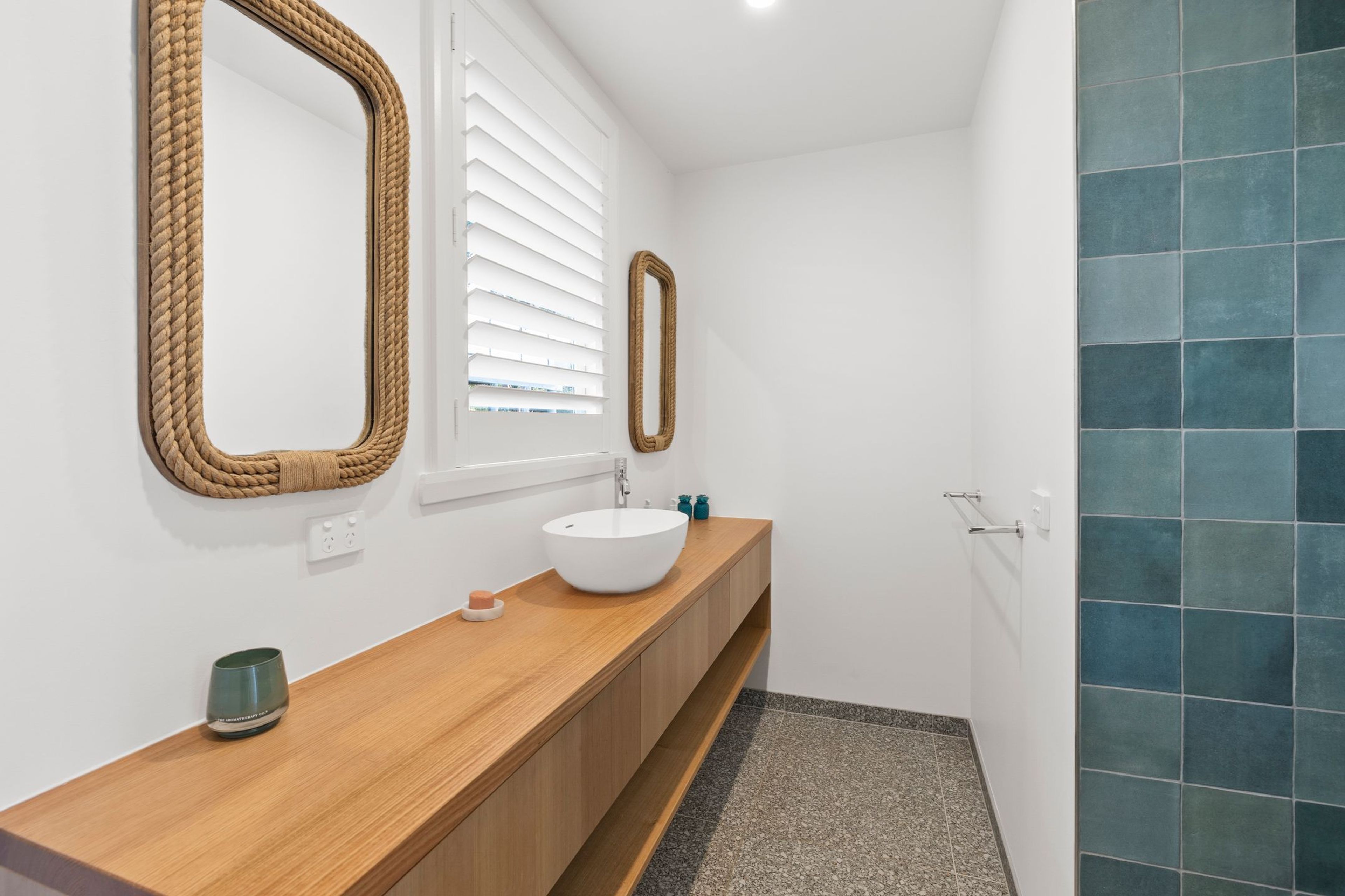 Ein Badezimmer mit einem Holzbadezimmerhocker, einem weißen Waschbecken und zwei Spiegeln mit Seilrahmen.