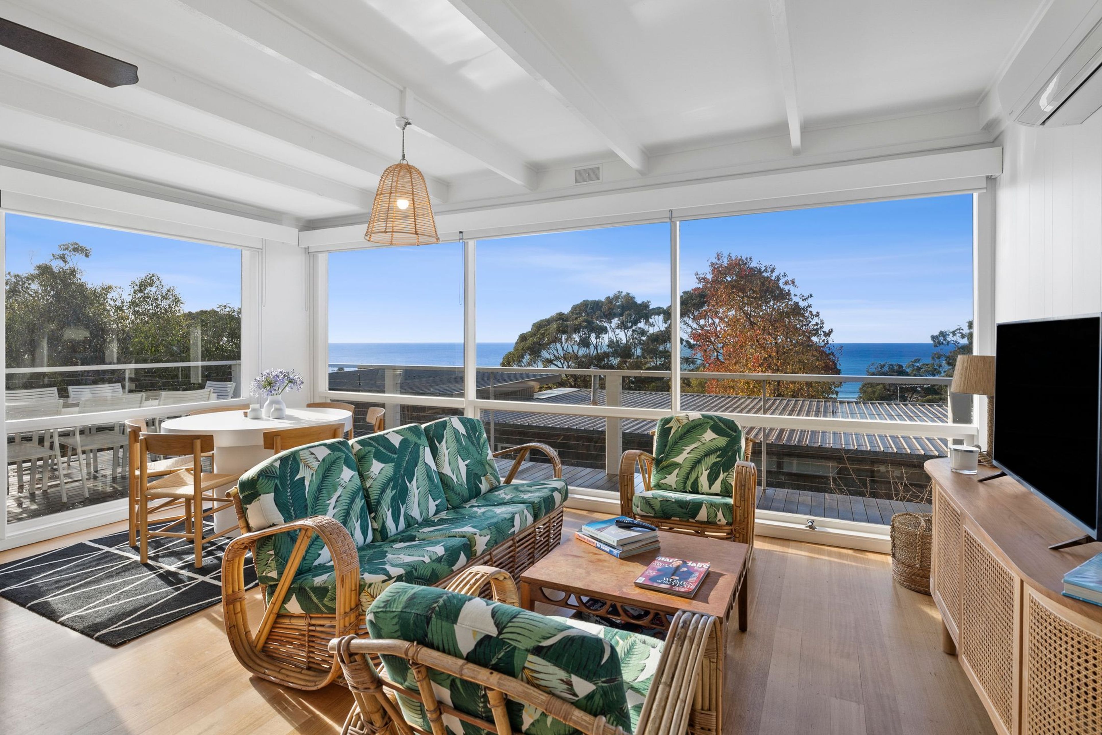 Un balcon spacieux offrant une vue sur la mer et les arbres, aménagé avec des fauteuils en osier et un canapé.