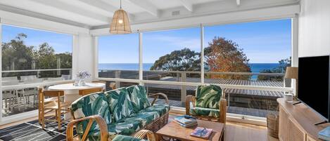 A spacious balcony with a view of the sea and trees, furnished with wicker chairs and a sofa.