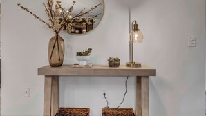 Een houten console tafel met een spiegel, een vaas met takken en twee kleine potplanten.