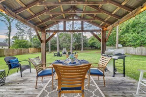 A covered outdoor patio with a wooden table set for dining, surrounded by chairs, and a grill. - Quiet escape in Wilmington (Wilmington)