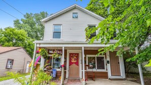 A two-story house with a front porch, a red door, and a small window above the door.