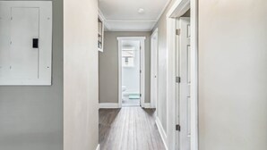 A hallway with a light switch on the left, a door at the end, and a light fixture on the ceiling.
