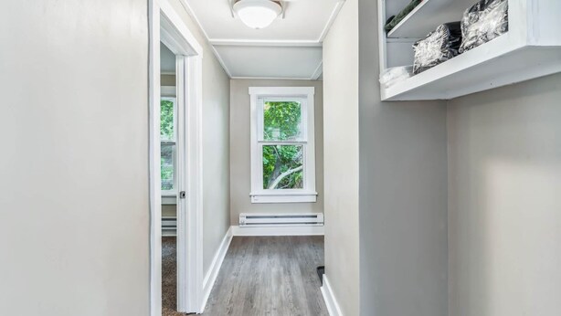 A narrow hallway with a window, a radiator, and a shelf with items on it.