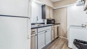 A compact kitchen with white cabinets, a microwave, a sink, and a small trash bin.