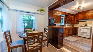 A kitchen with wooden cabinets, a stove, and a dining area with a table and chairs. - The Dutch Getaway (Pensacola)
