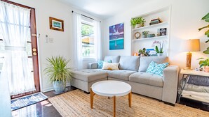 A modern living room with a grey sectional sofa, a round coffee table, and a bookshelf with plants and books. - The Dutch Getaway (Pensacola)