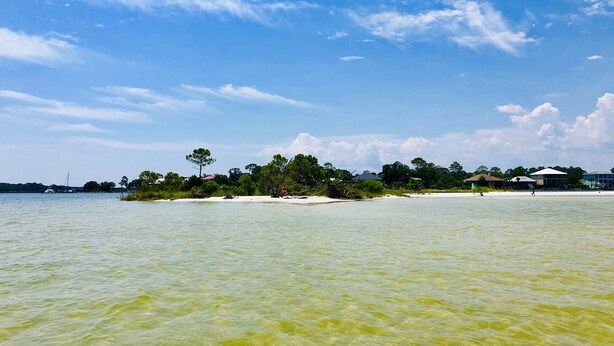 A beach with clear water, a small island with trees, and buildings in the background. - The Dutch Getaway (Pensacola)