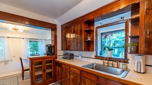 A kitchen with wooden cabinets, a sink, and a window with a view of greenery. - The Dutch Getaway (Pensacola)