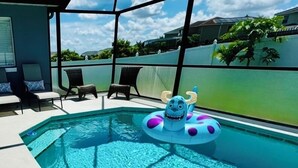 A swimming pool with a blue inflatable toy, lounge chairs, and a view of a green fence and houses in the background. - New! Themed rooms, Heated pool with private fenced yard, Pet friendly! (Davenport)