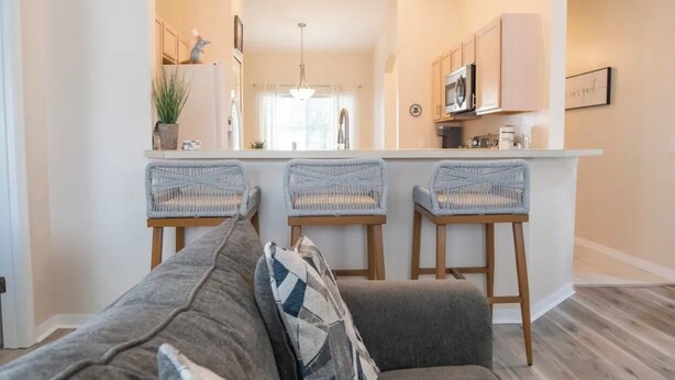 A modern kitchen with a central island, three wicker bar stools, and a grey sofa with a patterned throw pillow. - New! Themed rooms, Heated pool with private fenced yard, Pet friendly! (Davenport)