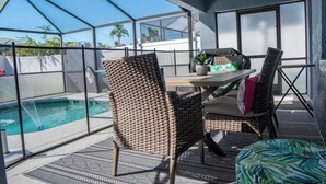 A covered outdoor area with a pool, wicker chairs, a table, and a view of the surrounding landscape. - New! Themed rooms, Heated pool with private fenced yard, Pet friendly! (Davenport)