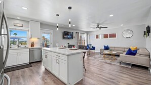 Une cuisine moderne avec des meubles blancs, un îlot central et un coin repas comprenant un canapé et une table basse.