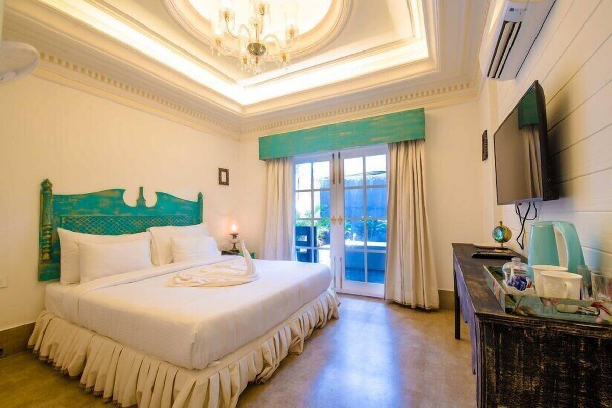 Quarto de hotel com cama grande, lustre, televisão e vista para o exterior.