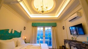 Habitación de hotel con una cama grande, un candelabro, un televisor y vistas al exterior.