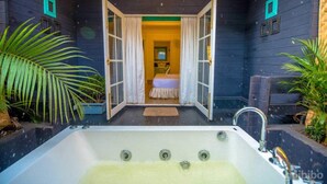 Habitación con una bañera grande, una cama con cubrecama blanco y vista a otra habitación por un umbral abierto.