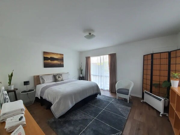 A modern bedroom with a large bed, a chair, a radiator, and a view of the outdoors.