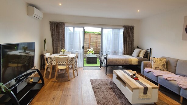 A modern living room with a flat-screen TV, a dining table with chairs, a sofa, and a large window with curtains.