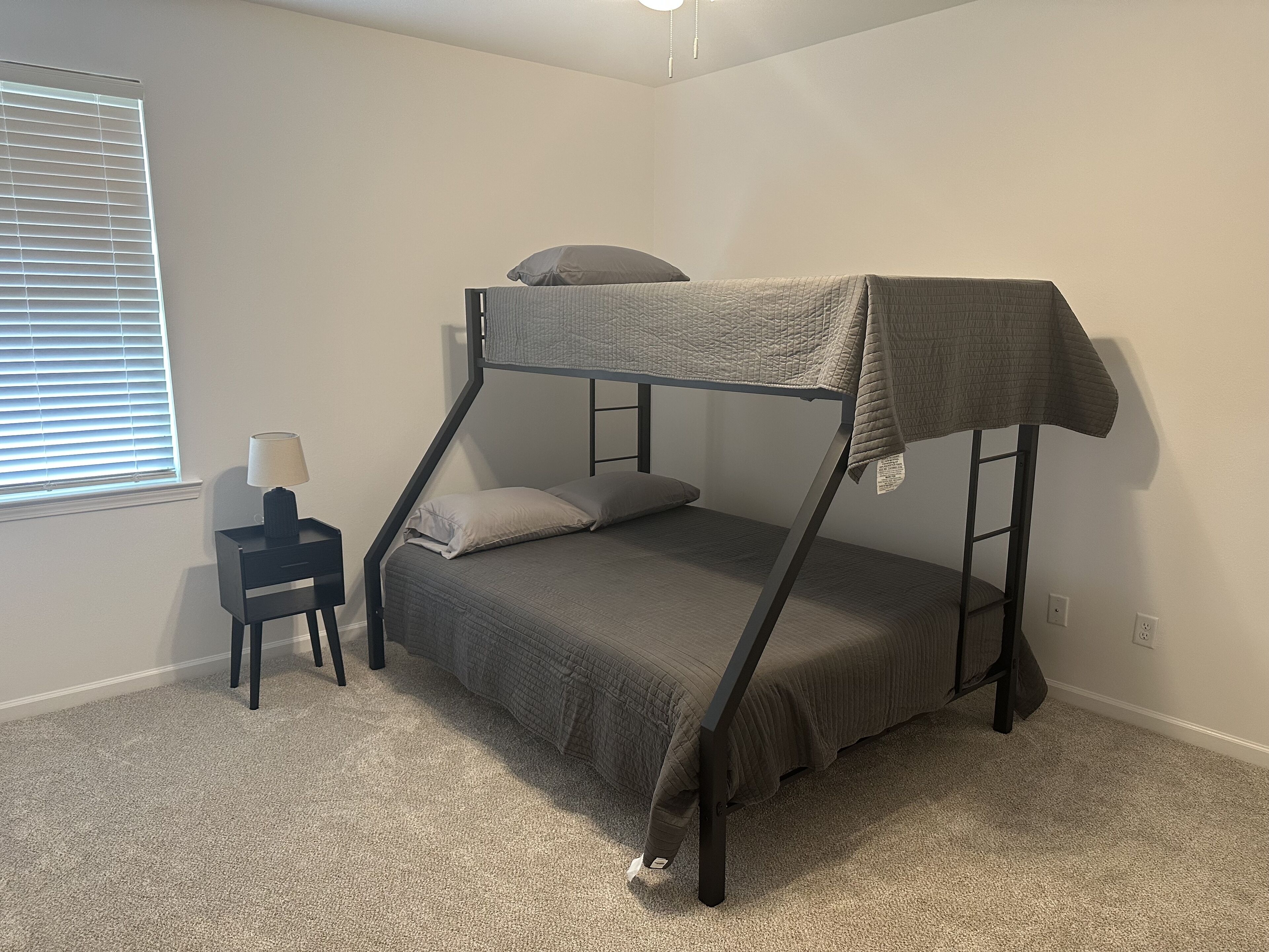 A bunk bed in a room with a small bedside table and a lamp.