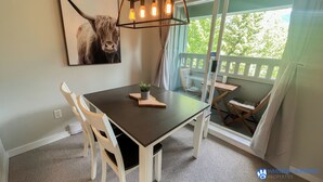 A dining area with a dark wooden table, white chairs, a potted plant, and a framed artwork of a bull. - Renovated Whistler Village Condo with Stunning Blackcomb Views (Whistler)