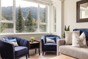 A room with two armchairs, a sofa, and a view of a mountainous landscape through large windows.