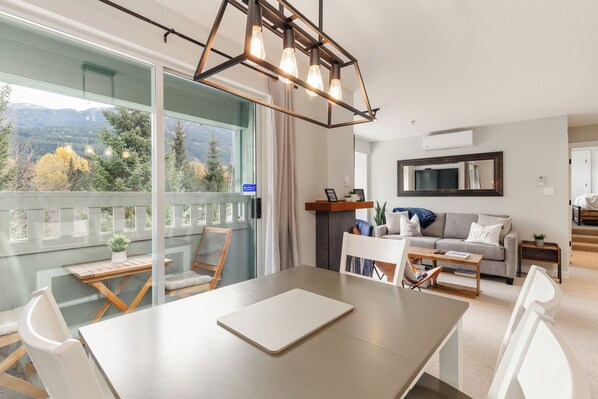 A modern living room with a balcony, a dining area, and a view of the mountains.