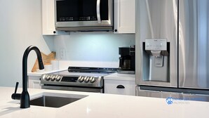 A modern kitchen with a stainless steel refrigerator, a built-in microwave, a coffee maker, and a sink with a faucet. - Renovated Whistler Village Condo with Stunning Blackcomb Views (Whistler)